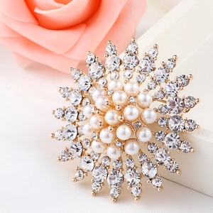 Elegant floral pearl brooch with gold base and sparkling crystals on a rose background
