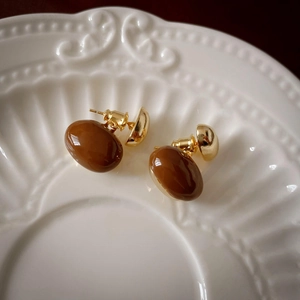 Macro detail of vintage brown drip oil bean earrings on white embossed ceramic plate