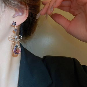 Detailed close-up of a long silver bow earring featuring a faceted purple drop gemstone