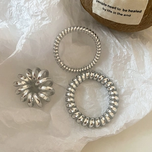 Close-up of three silver spiral hair ties with metallic finish on white textured paper