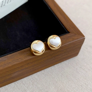 Macro shot of gold heart earrings with white mother of pearl inlay on velvet box
