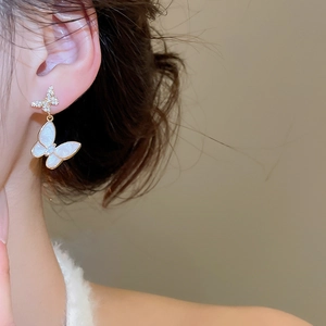 Close-up of butterfly earrings with gold zircon studs and white pearlescent wings