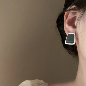 Close-up of geometric square resin stud earrings in black and gold on model