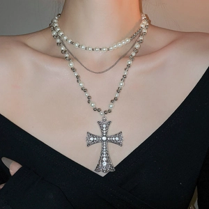 Detailed close-up of a three-layer necklace with pearl beads and a crystal gothic cross