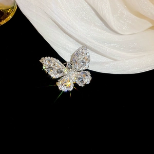 Macro shot of silver butterfly brooch with teardrop zircons on white silk background