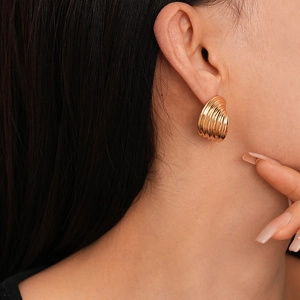 Close-up of a model wearing a golden spiral striped metal earring with a shell texture