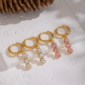 Elegant gold earrings with white and pink zircon charms on a textured stone background