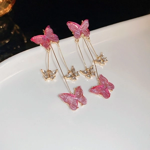 Détail de boucles d'oreilles papillon dégradé rose avec de longs glands métalliques