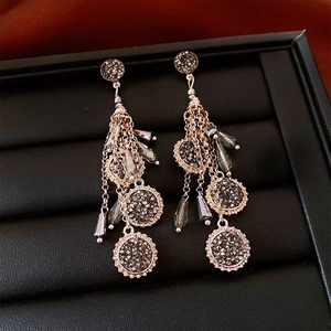 Détail de boucles d'oreilles à pompons dorés avec cristaux gris et chaînes en métal