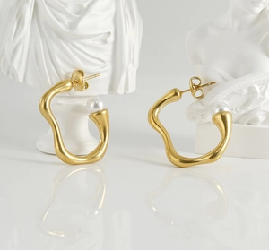 Détail de boucles d'oreilles dorées irrégulières avec perle sur buste en plâtre blanc