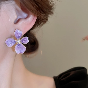 Detail of purple enamel flower earring with pearl center on ear of a female model
