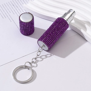 Detail shot of purple rhinestone perfume spray bottle with silver keychain on white background
