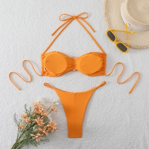 Flat lay of bright orange bikini set with metal ring detail on white plush rug