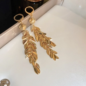 Close-up of gold flower tassel earrings with leaf-shaped charms in a white jewelry box