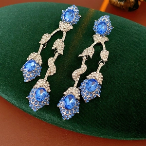 Close-up of vintage flower earrings with blue oval gems on dark green velvet padding