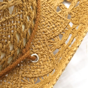 Detail of woven straw hat featuring a silver metal eyelet and dark brown drawstring