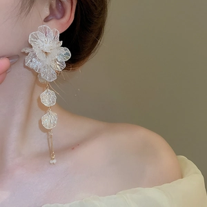 Close-up of white acrylic flower tassel earrings with golden chains on a model