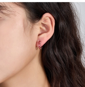 Close-up of S925 silver hoop earrings with red enamel hearts on female model's ear