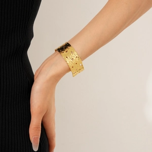 Detail of wide hammered gold cuff bracelet with hollow cutouts on model wrist