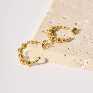 Detail view of golden beaded C-shaped earrings on a textured travertine stone surface