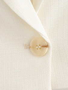 Macro shot of a beige four-hole button on high-quality off-white linen blend fabric