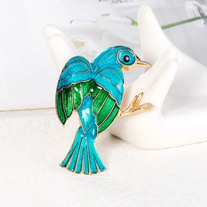 Elegant bird brooch in blue and green enamel with gold plating on a white display stand