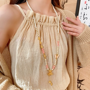 Detailed shot of long pearl necklace with pink butterfly and tassel gourd pendant