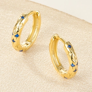 Macro view of gold hoop earrings with star engravings and blue zircon stones