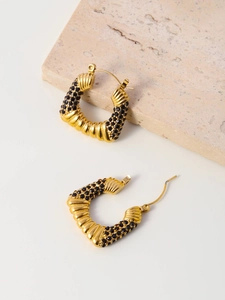 Detail view of gold C-shaped earrings with black zircon stones on a natural stone base
