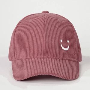 Detailed close-up of pink corduroy baseball cap featuring a white embroidered smiley face