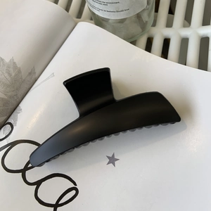 Close-up of a large matte black hair claw clip resting on a white book with soft lighting