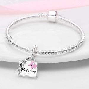 Macro shot of silver shopping bag charm with pink bow and Shopping engraving on bracelet