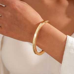 Detail eines goldenen Harz-Metallarmbands mit Hammerschlag-Textur am Handgelenk