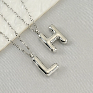 Polished silver bubble initial necklaces with H and L pendants on grey fabric background