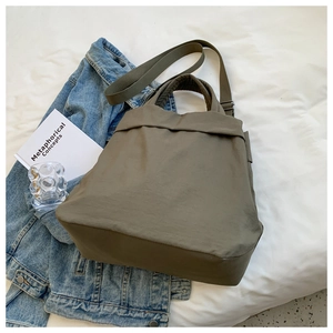 Flat lay of army green nylon tote bag on white sheet with lifestyle props and books