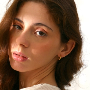 Detail of twisted spiral gold stud earrings worn by model for a vintage french aesthetic look