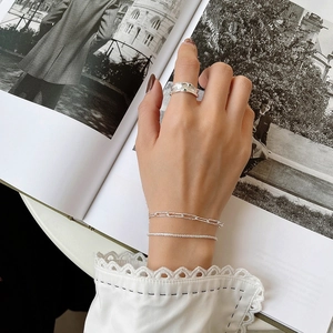 Dettaglio del bracciale a catena in argento S925 e anello testurizzato su mano donna