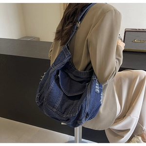 Sac à épaule en jean bleu foncé avec bords effilochés et boucle en métal sur un modèle