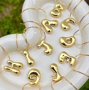 18K gold plated stainless steel bubble letter necklaces on a wavy white tray