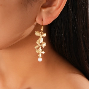 Close-up of golden floral drop earring with white pearl on a model for a vintage look