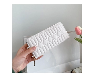 Close-up of white quilted long wallet with gold zipper, held near a gift bag and tulips