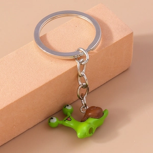 Detailed view of a cute green and brown snail keychain on a minimal orange platform