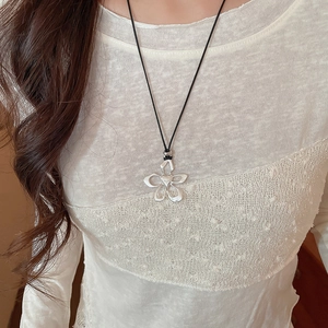 Detailed view of silver flower pendant with heart relief on black cord over white lace