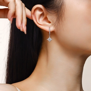 Detailed close-up of a silver star drop earring with sparkling moissanite stones on a model