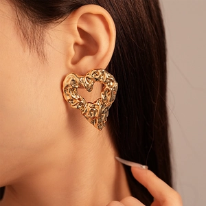 Close-up of gold hollow heart earrings with textured lava metal finish on model
