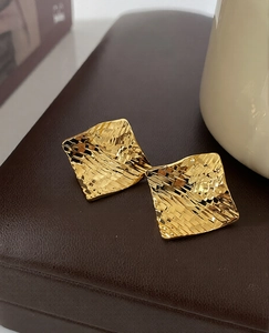 Macro shot of gold plated square earrings with textured rhombic pattern and metallic finish