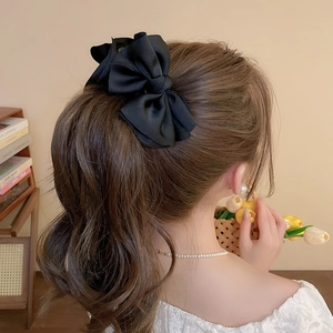 Detail of oversized black satin bow hair clip styled on an elegant ponytail