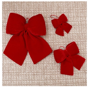 Close-up of three sizes of red velvet Christmas bows with hanging strings on a textured rug