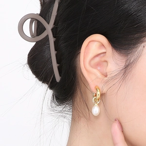 Gros plan d'un modèle portant une boucle d'oreille en C dorée avec une perle ovale blanche