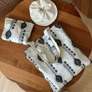 Detailed set of embroidered cotton linen tote bag with matching pouch and hair tie on wood